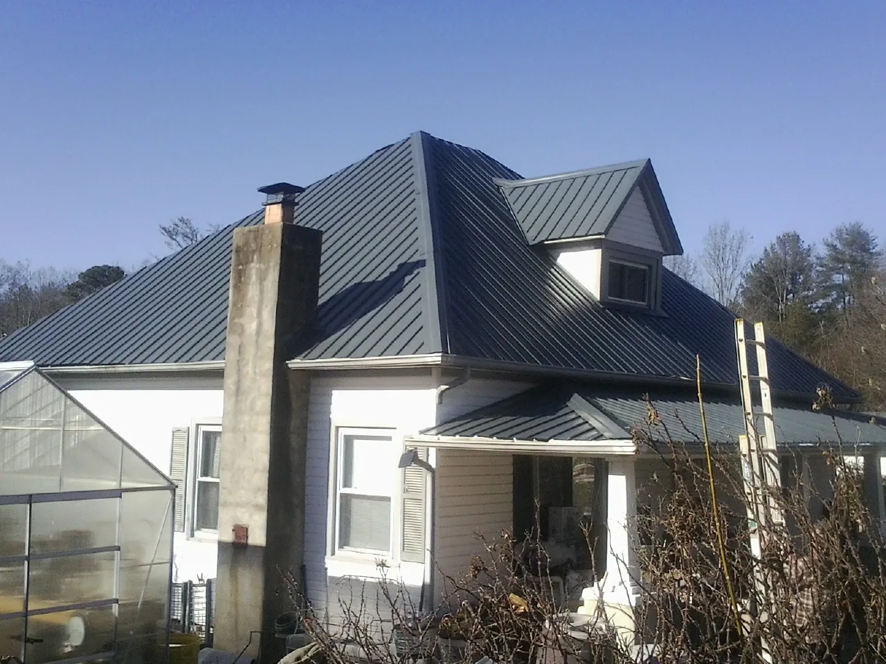 Dark blue standing seam metal roof on a white farmhouse with dormer — Slate & Tile Roof Repair by Roofing Brothers in De Mossville