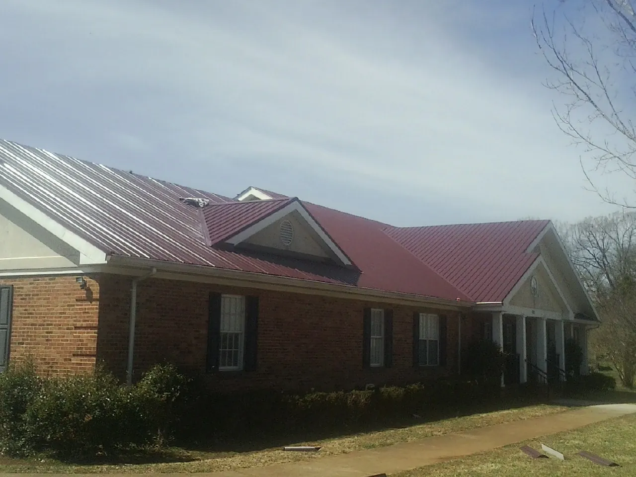 Red metal roof with gabled entries on a long brick building, from a Hail Damage Roof Repair job in De Mossville