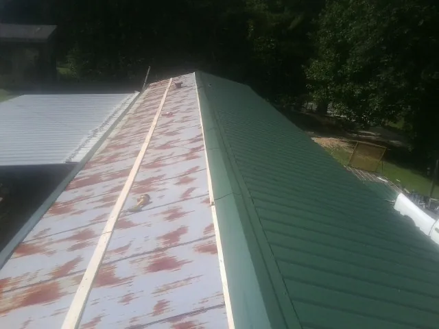 Old rusted panels beside newly installed green metal roofing — Wind Damage Roof Repair by Roofing Brothers in De Mossville
