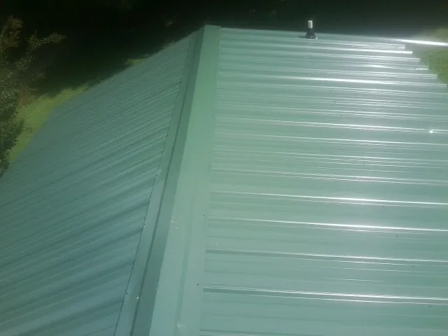 New green metal panels meeting at the ridge of a roof — Flat Roof Repair work by our crew in De Mossville