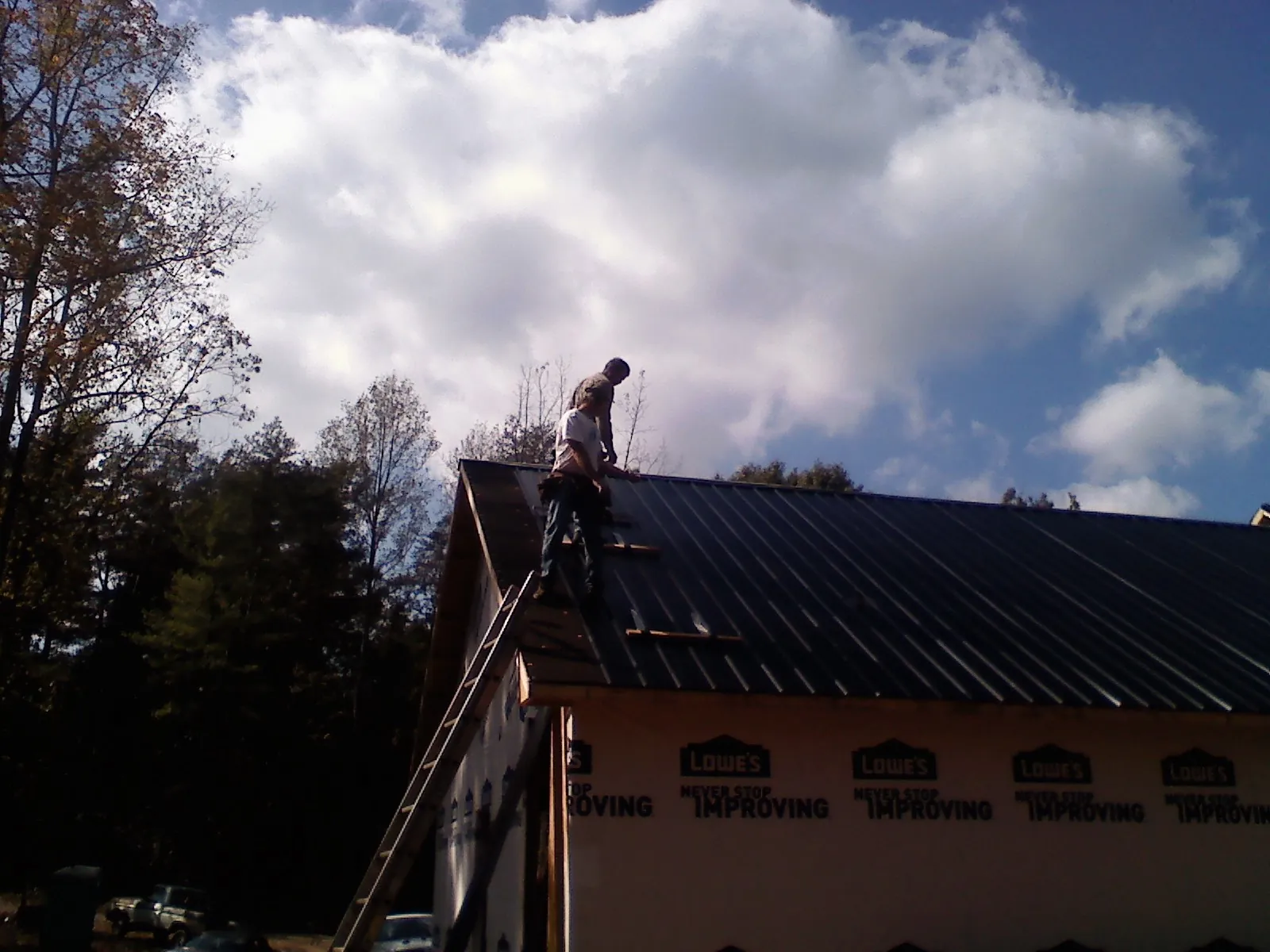 Roofer fastening dark metal panels high against a cloudy sky, from a Roof Inspection job in De Mossville