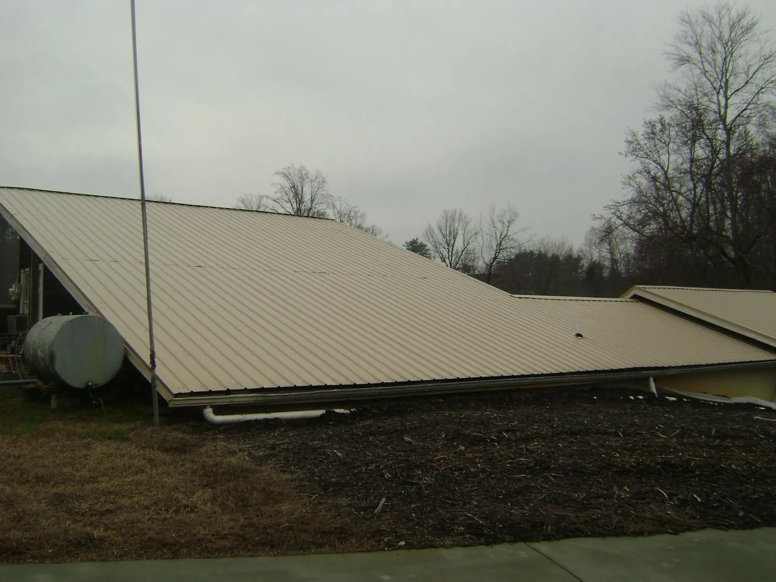 Wide tan metal roof plane seen from the ground beside a propane tank in De Mossville
