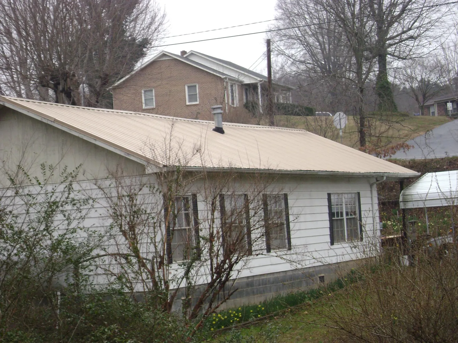 Tan metal roof on a white sided house set into a hillside — Commercial Roofing by Roofing Brothers in De Mossville
