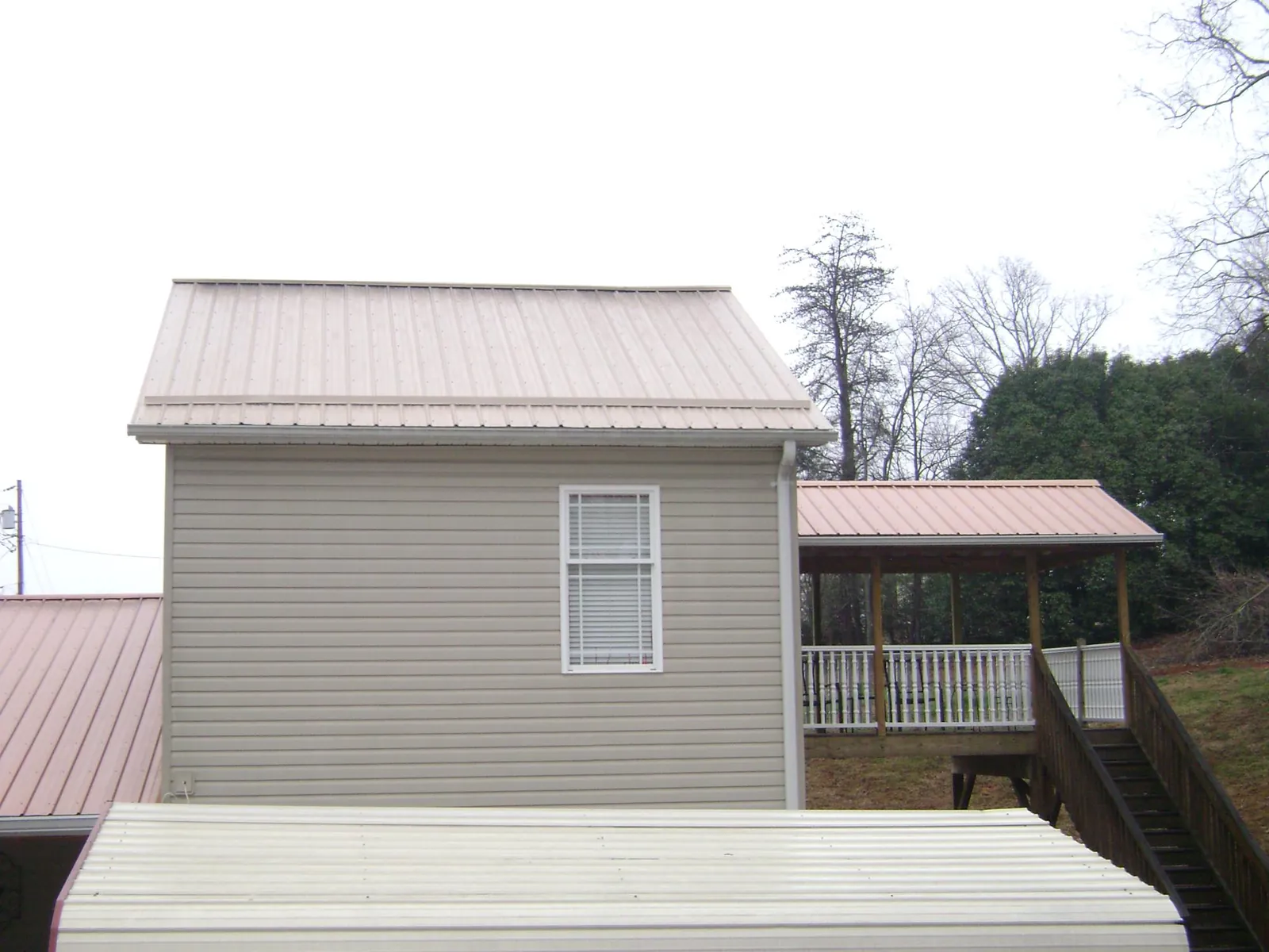 Tan metal roofs on a two story addition and attached porch, from a Roof Replacement job in De Mossville